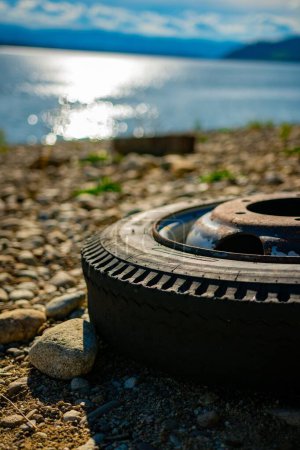 Foto de Un primer plano vertical de una rueda de coche vieja y oxidada parcialmente vista en una orilla junto al mar - Imagen libre de derechos