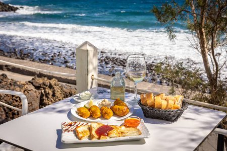 Foto de Un primer plano de comida rápida frita y tostadas francesas sobre una mesa blanca con un fondo de un mar - Imagen libre de derechos