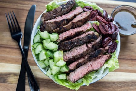 Photo for A top view of the steak salad on a white plate with a sauce on a wooden board - Royalty Free Image