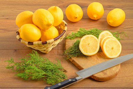 Téléchargez les photos : Un gros plan de citrons dans un panier en osier et d'autres citrons sur une planche à découper avec un couteau - en image libre de droit