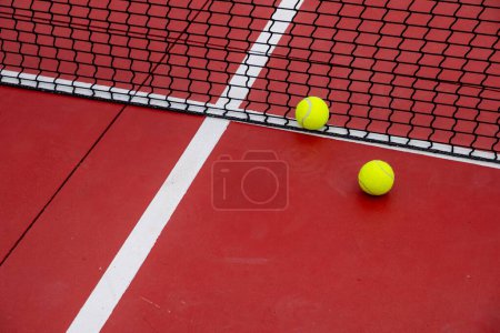 Téléchargez les photos : Les deux balles de tennis reposant au filet et les lignes de court sur un court en béton rouge - en image libre de droit