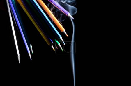 Photo for Closeup of colored pencils in different directions on black background with white smoke coming from below, with copy space - Royalty Free Image
