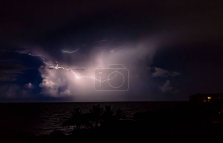 Téléchargez les photos : Une vue de nuit d'un océan sous le ciel mauve envoûtant avec la foudre - en image libre de droit