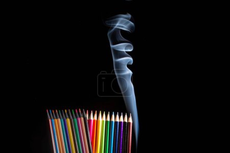 Téléchargez les photos : Un gros plan de crayons de couleur groupés sur fond noir avec de la fumée blanche venant d'en bas, avec de l'espace de copie - en image libre de droit