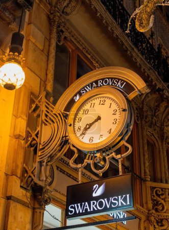 Téléchargez les photos : Un plan de nuit à angle bas d'une horloge le logo de bijoux Swarovski devant leur magasin à Budapest - en image libre de droit