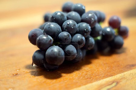 Téléchargez les photos : Un gros plan est fraîchement lavé raisins noirs avec des gouttes d'eau sur elle sur une table en bois - en image libre de droit