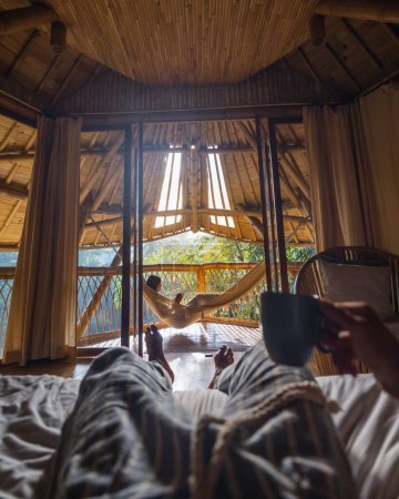 Téléchargez les photos : Un plan vertical des jambes masculines allongées dans le lit avec une femelle allongée sur un hamac sur le balcon en arrière-plan - en image libre de droit