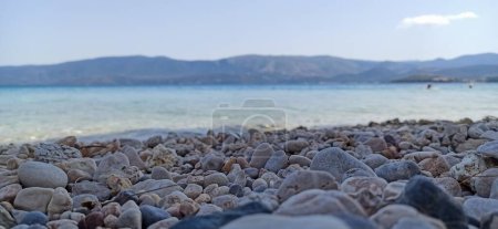 Téléchargez les photos : Un gros plan de la côte graveleuse sur la plage avec la mer et les montagnes en arrière-plan - en image libre de droit