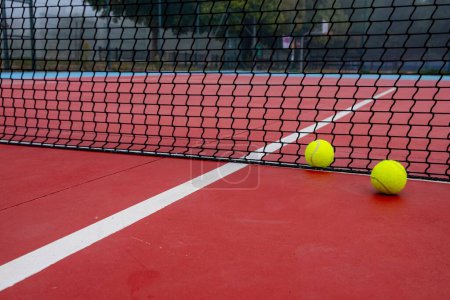 Foto de Las dos pelotas de tenis descansando junto a la red y las líneas de la cancha en una cancha de hormigón rojo - Imagen libre de derechos