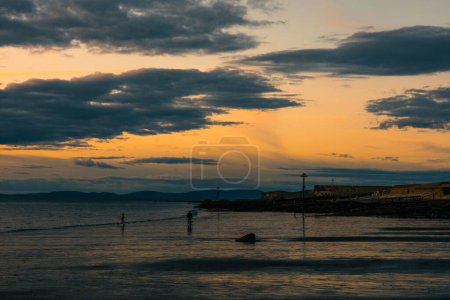 Téléchargez les photos : Les gens marchant sur le rivage au coucher du soleil avec un ciel nuageux en arrière-plan - en image libre de droit