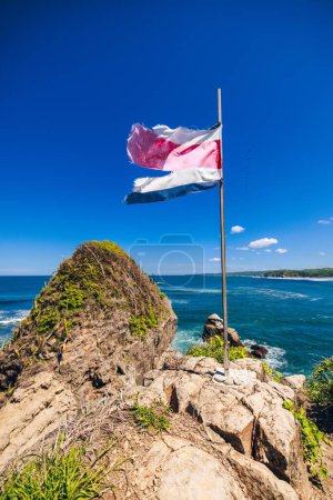 Foto de Un disparo vertical de la bandera halagadora de Costa Rica con el océano azul en el fondo - Imagen libre de derechos