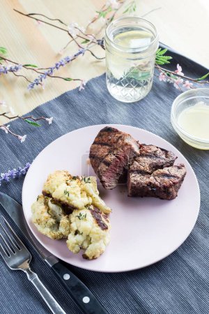 Téléchargez les photos : Un plan vertical du steak dîner sur une assiette blanche avec une sauce et un verre d'eau sur un tissu bleu - en image libre de droit