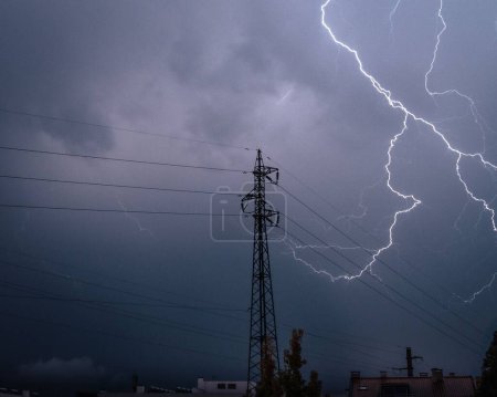 Photo for The lightning striking above a transmission tower on a dark gloomy and cloudy evening - Royalty Free Image