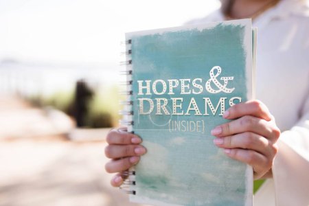 Photo for A closeup view of female hands holding a notebook with a writing "Hopes and Dreams" on a front page - Royalty Free Image