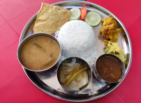 Assamese vegetarian thali containing plain rice, yellow dal with tomato, boiled vegetables, khar, mashed potatoes, vegetable fry, salad and papad.