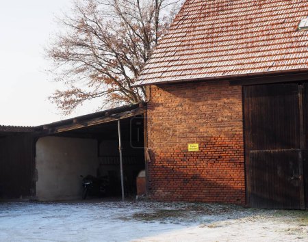 Foto de Un antiguo granero de ladrillo con puerta de madera y amarillo no hay señal de aparcamiento en alemán y motocicleta estacionada debajo de la cochera en invierno - Imagen libre de derechos