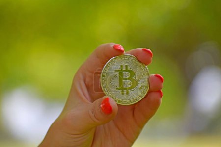 Téléchargez les photos : Un gros plan d'une femme tenant une pièce de monnaie Bitcoin or sur un fond flou - en image libre de droit