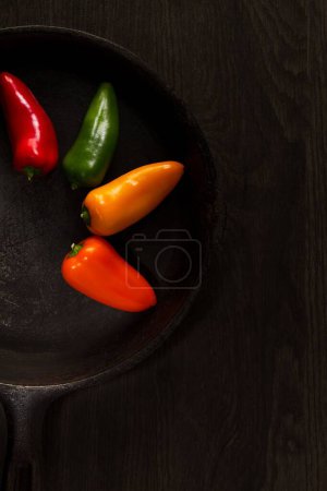 Téléchargez les photos : Un plan vertical de quatre poivrons colorés isolés sur une casserole noire en cercle - en image libre de droit