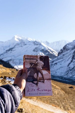 Téléchargez les photos : Un gros plan de la main d'une personne tenant un livre de coureur de cerf-volant contre une énorme montagne - en image libre de droit
