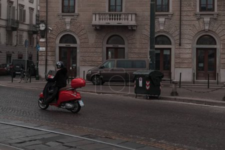 Téléchargez les photos : Un homme chevauchant un cyclomoteur rouge dans l'étroite rue carrelée de Turin en hiver - en image libre de droit