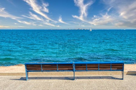 Téléchargez les photos : Un banc bleu vide au bord d'un beau lac bleu par une journée ensoleillée - en image libre de droit