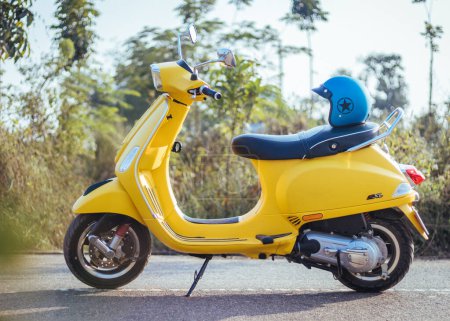 Photo for A closeup view of a beautiful yellow Vespa SXL 125 with a blue helmet in a street - Royalty Free Image