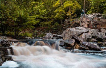 Photo for A long exposure shot of a waterfall in a forest with a hiker sitting on a rock in the background - Royalty Free Image