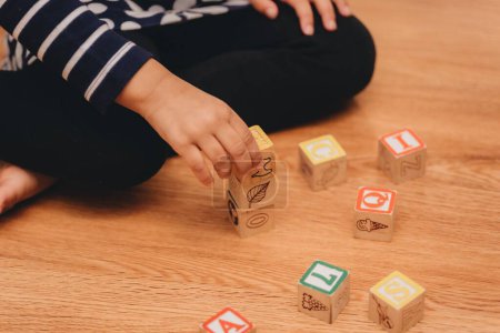 Téléchargez les photos : Une fille d'âge préscolaire, jouant avec des blocs de lettres en bois à la maison sur le plancher de bois franc, le concept de l'éducation préscolaire - en image libre de droit