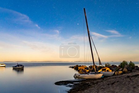 Téléchargez les photos : Un beau cliché de bateaux amarrés sur la plage la nuit avec ciel étoilé bleu nuageux, Allemagne. - en image libre de droit