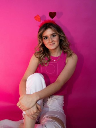 Foto de Un retrato de cerca de una hermosa joven posando con una diadema con corazones sobre un fondo rosa - Imagen libre de derechos