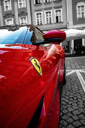 Foto de Una vista lateral vertical de un coche Ferrari rojo brillante estacionado en una calle y su logotipo - Imagen libre de derechos