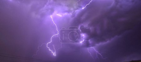 Photo for A panoramic view of lightning illuminating the dark purple cloudy sky - Royalty Free Image