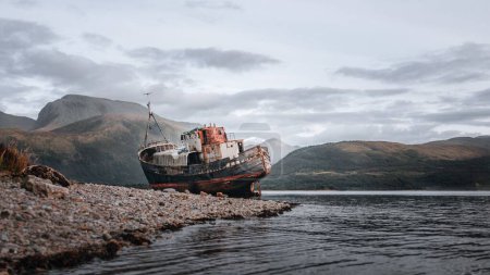 Téléchargez les photos : Un vieux navire abandonné sur la côte de la ville de Fort William en Écosse entouré de collines - en image libre de droit