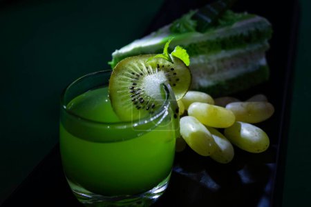 Téléchargez les photos : Un gros plan d'un verre de boisson verte avec un kiwi, des raisins et une pâtisserie sur une planche - en image libre de droit