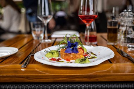 Photo for A closeup shot of a Salmon tartare decorated by a blue flower on a wooden table in a restaurant - Royalty Free Image