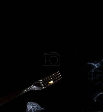 Téléchargez les photos : Gros plan d'une fourchette argentée sur un fond noir avec de la fumée venant d'en bas - en image libre de droit