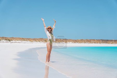 Téléchargez les photos : Une femme caucasienne avec un chapeau de paille posant sur une plage de sable contre la mer bleue par une journée ensoleillée - en image libre de droit