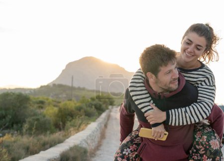 Photo for A couple in piggyback looking at the horizon during sunset - Royalty Free Image