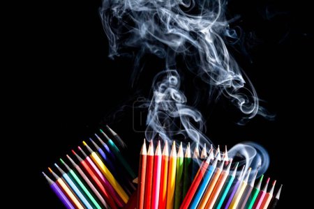 Foto de Un primer plano de lápices de colores agrupados sobre fondo negro con humo blanco procedente de abajo, con espacio para copiar - Imagen libre de derechos