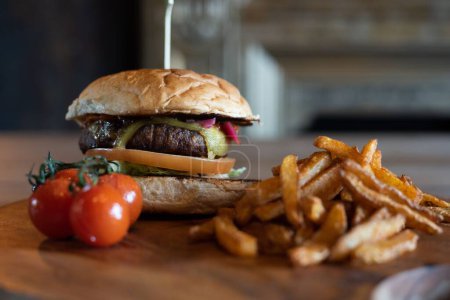 Foto de Una deliciosa hamburguesa y papas fritas en una tabla de madera con tomates cherry - Imagen libre de derechos