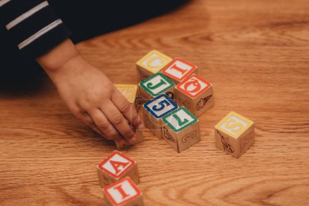 Téléchargez les photos : Une fille d'âge préscolaire, jouant avec des blocs de lettres en bois à la maison sur le plancher de bois franc, le concept de l'éducation préscolaire - en image libre de droit