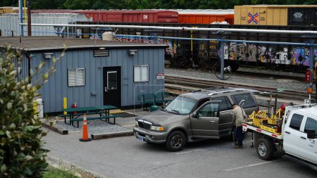 Téléchargez les photos : Plan éloigné d'une gare de triage, d'une personne qui travaille et de wagons garés près d'un bâtiment métallique - en image libre de droit
