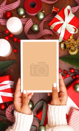 Foto de Un plano vertical de un marco vacío en una mano femenina sobre las decoraciones navideñas - Imagen libre de derechos