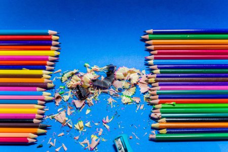 Téléchargez les photos : Un gros plan de rangée de crayons de bois colorés et de restes aiguisés isolés sur fond bleu - en image libre de droit
