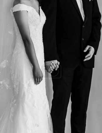 Photo for A vertical grayscale of the bridegroom and the bride holding hands on the wedding ceremony - Royalty Free Image