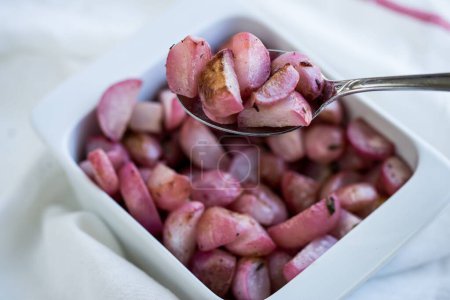 Photo for A closeup of the silver spoon with red sliced potatoes with the background of a bowl of red sliced potatoes on a white fabric during the daytime - Royalty Free Image