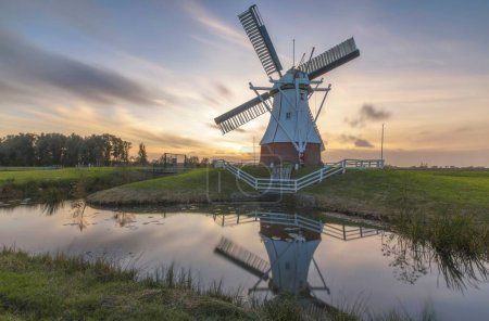 Téléchargez les photos : Vue d'un moulin à vent près de la rivière au coucher du soleil à Groningue, Allemagne - en image libre de droit