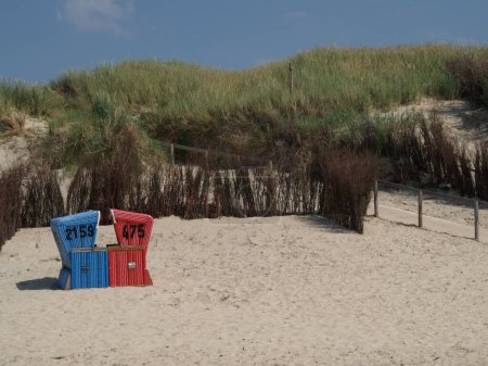 Téléchargez les photos : Chaises de plage à capuchon, sur la plage de l'île Langeoog en mer du Nord, par une journée nuageuse, et herbe verte en arrière-plan - en image libre de droit