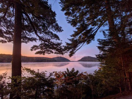 Téléchargez les photos : Une vue panoramique sur la forêt verdoyante et les collines qui se reflètent sur un lac tranquille au coucher du soleil brumeux - en image libre de droit