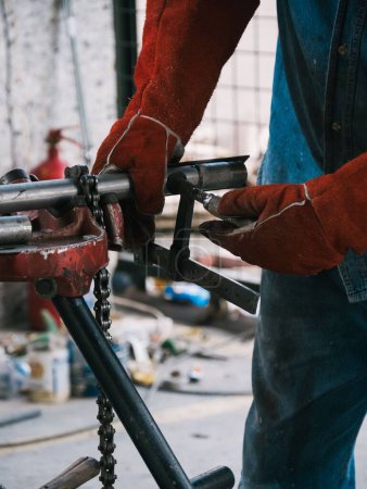 Foto de Un disparo vertical de un hombre que usa guantes que trabajan en equipos metálicos - el concepto de producción de metal artesanal - Imagen libre de derechos